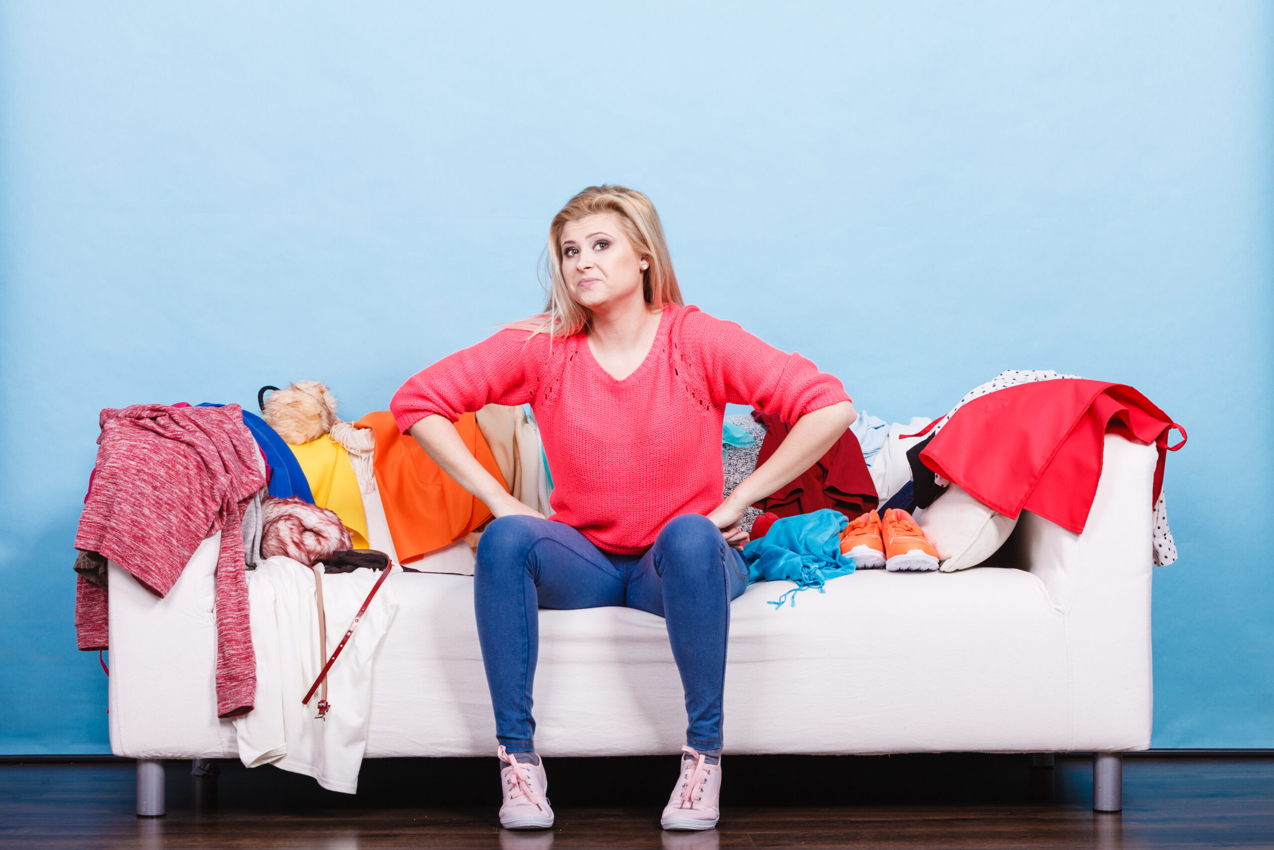 Frustrated woman sitting on couch covered with dirty laundry